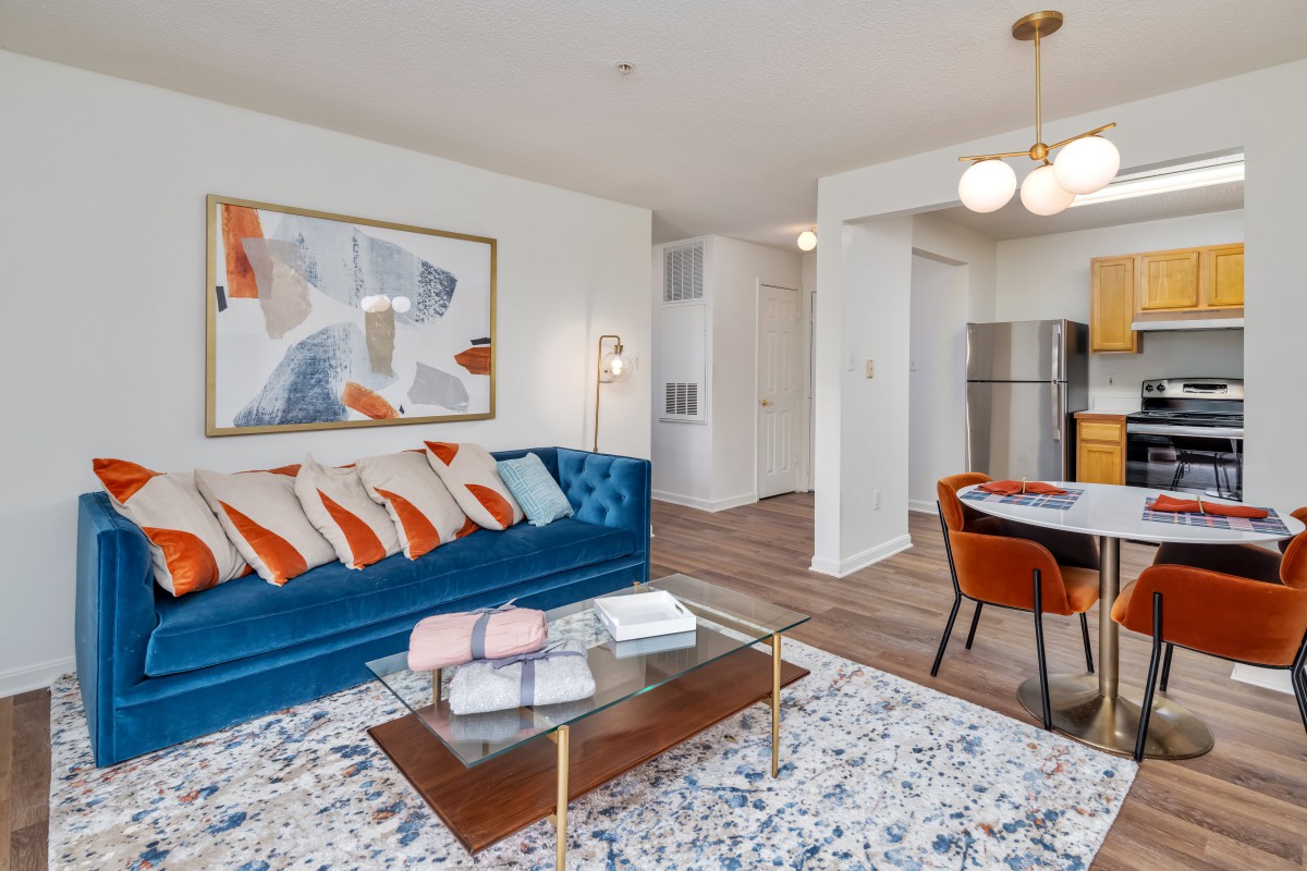 A modern living room and dining area with colorful decor, featuring a blue couch and abstract art.