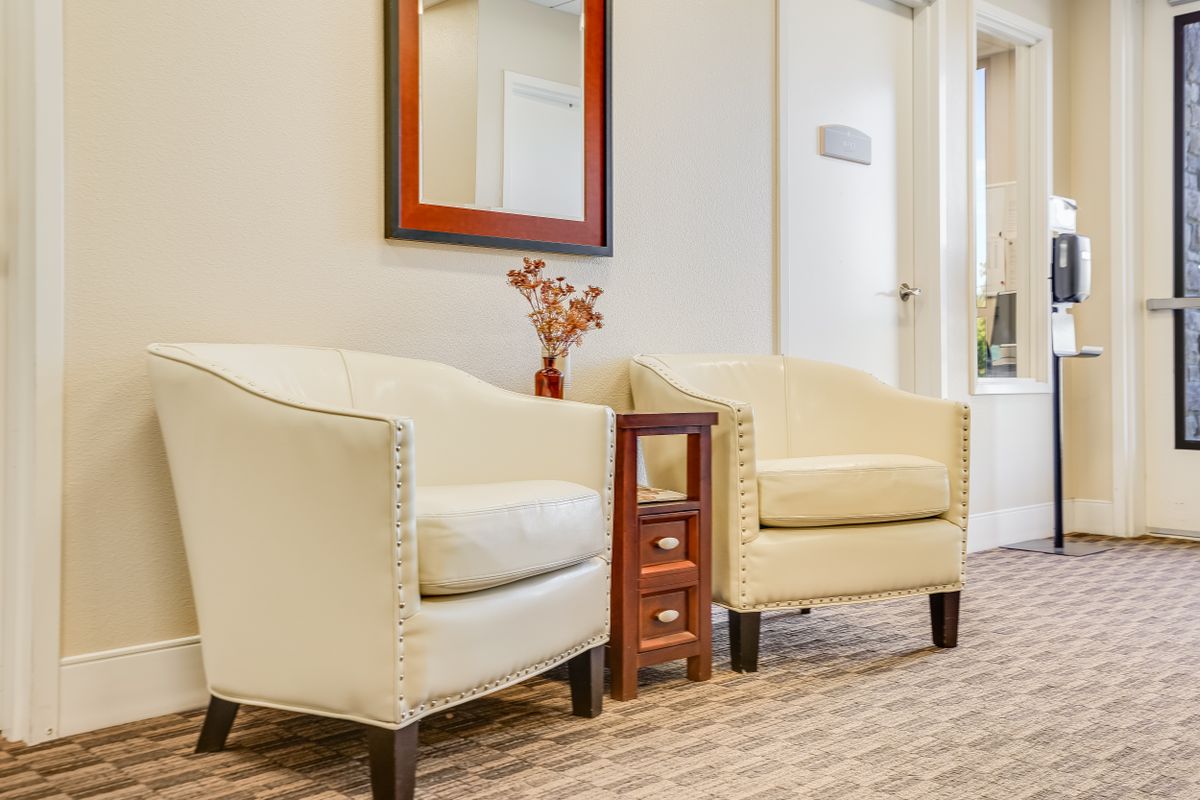 A cozy waiting room with two armchairs, a small table, and a decorative mirror.