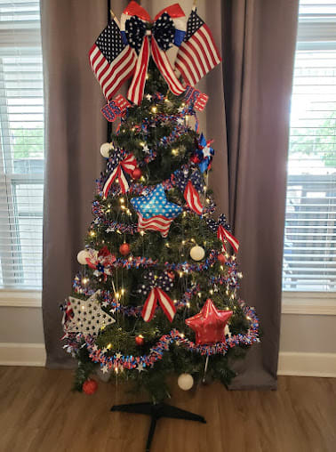 A Christmas tree decorated in a patriotic theme with red, white, and blue colors, featuring stars and ribbons.