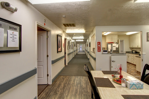 A well-lit hallway in a care facility, featuring doors leading to individual rooms and a dining area.