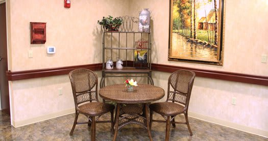 A cozy indoor corner featuring a rattan table and chairs with decorative shelving and artwork.