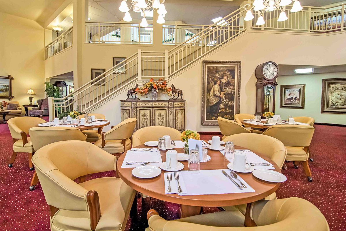 An elegant dining area with neatly set tables, classic decor, and a grand staircase.
