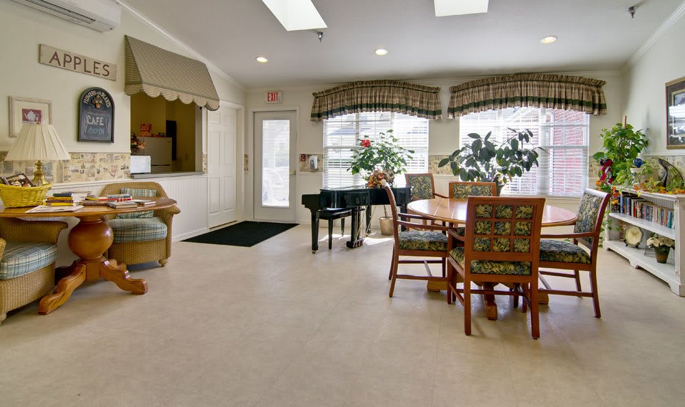 A bright interior room with a piano, table, chairs, and plants by the windows.
