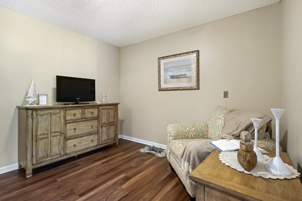 A cozy living room with a small TV on a wooden dresser, a couch, and a framed picture on the wall.