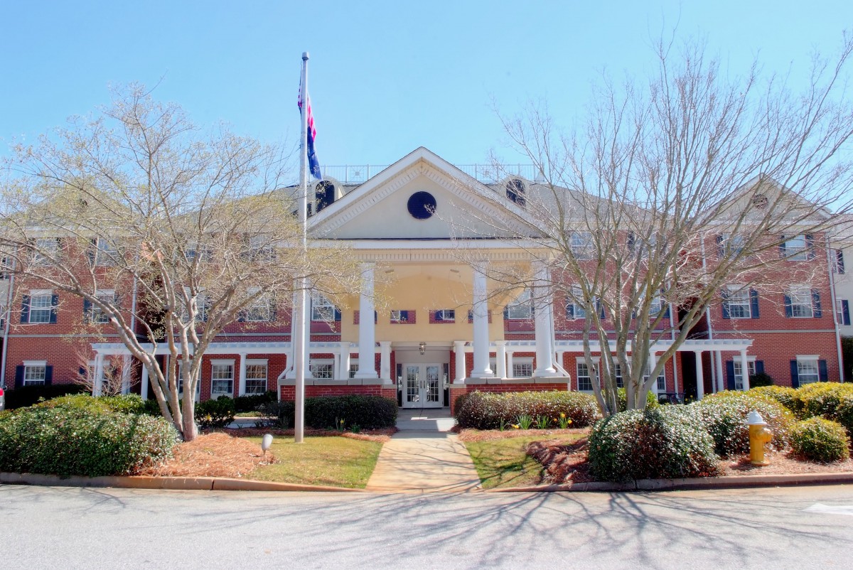 A grand building entrance with large columns and a flagpole, surrounded by landscaped greenery.