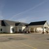 A single-story building with a gabled roof and an attached covered entrance, surrounded by a parking lot.