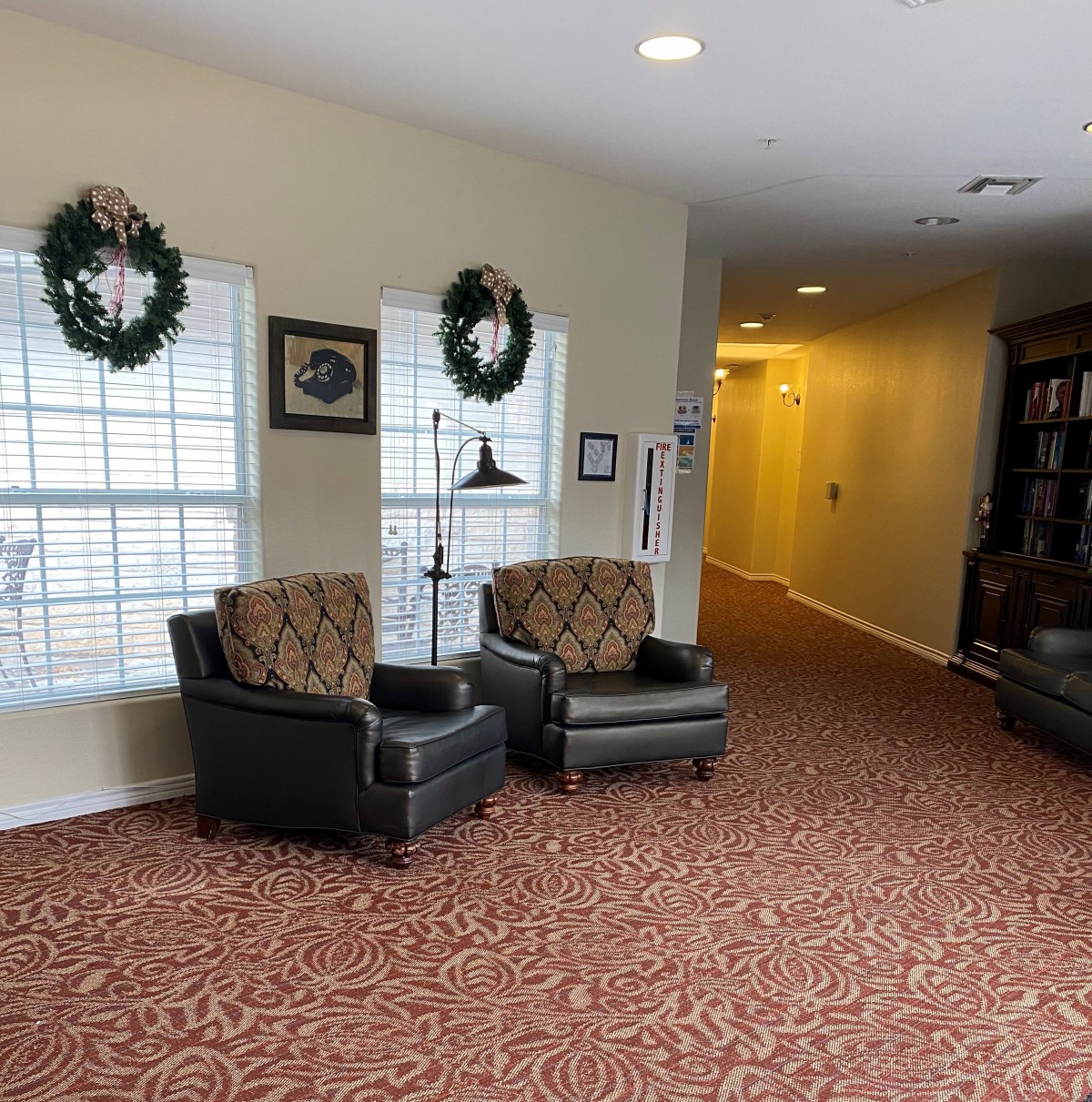 A cozy lobby area with patterned carpet, two armchairs, and holiday wreaths on the windows.