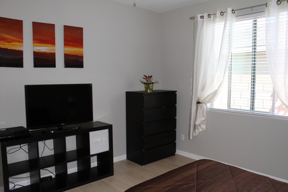 A minimalist bedroom with a dresser, television, and window with curtains.