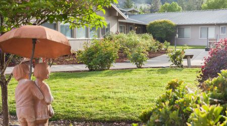 A serene outdoor view of a house with a lush green lawn and surrounding bushes.