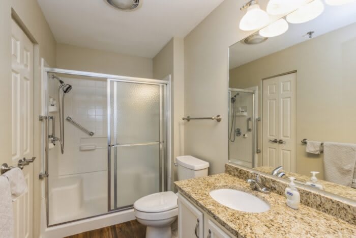 A modern bathroom featuring a glass shower enclosure, granite countertop with a sink, and a toilet.