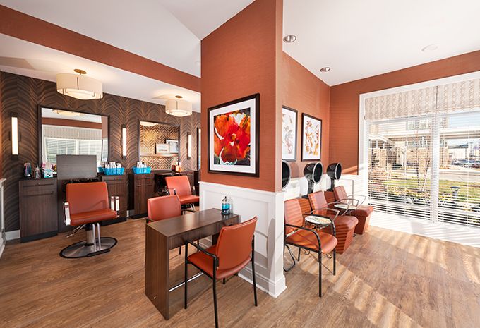 A modern salon interior featuring a waiting area with orange chairs, hair dryers, and vibrant artwork on the walls.