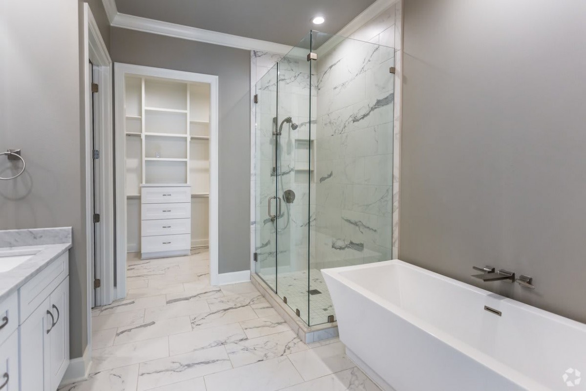 A modern bathroom featuring a glass-enclosed shower, standalone bathtub, and adjacent walk-in closet.