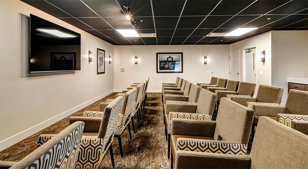 A small conference room with neatly arranged chairs facing a projector screen, accompanied by ambient lighting and wall dcor.