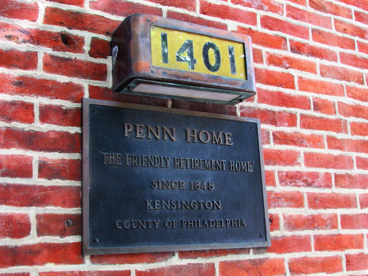 A building plaque and house number on a brick wall displaying 'Penn Home' and address details.