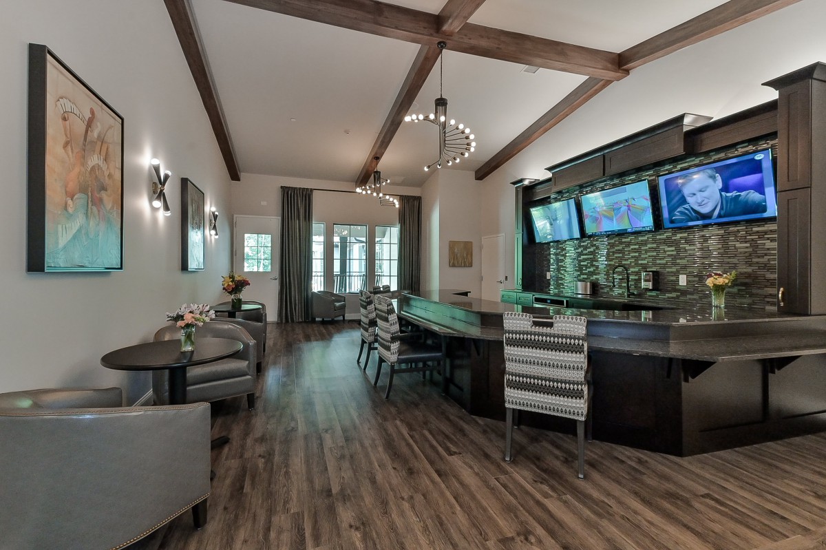 A modern bar area with wooden flooring, beamed ceiling, and multiple TV screens.