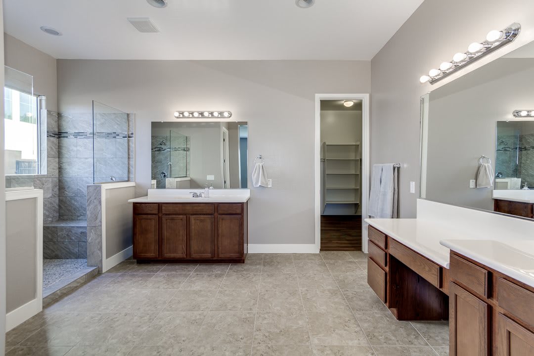 A spacious modern bathroom featuring a large mirror, wooden cabinets, and a walk-in closet.