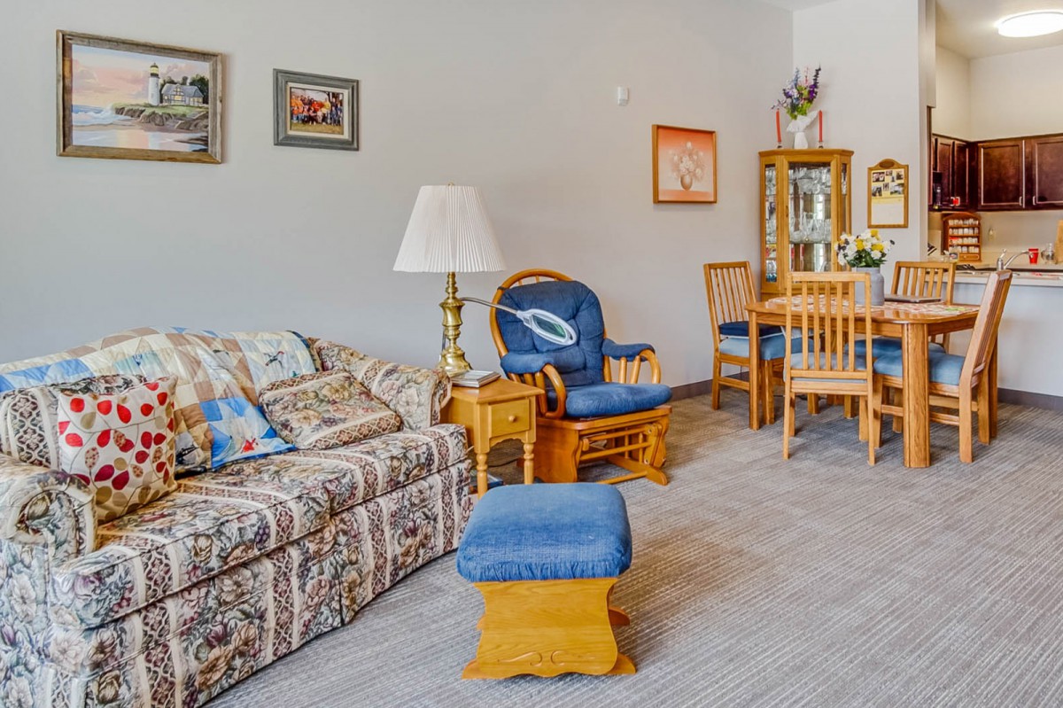 A cozy living room featuring a patterned sofa, blue cushioned armchair, and wooden dining set.