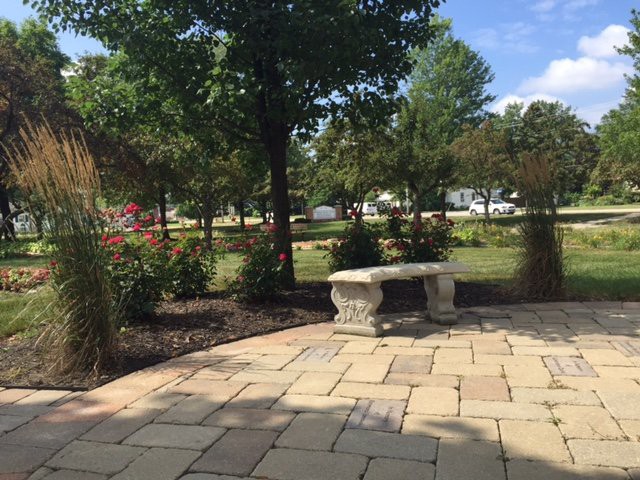 A peaceful park scene with a stone bench, surrounded by trees and flowers.