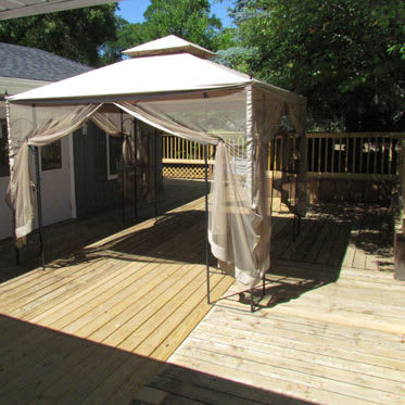 A gazebo with a canopy set up on a wooden deck under a sunny sky.