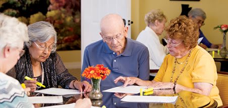 A group of elderly individuals engaged in reading and discussion at a table.