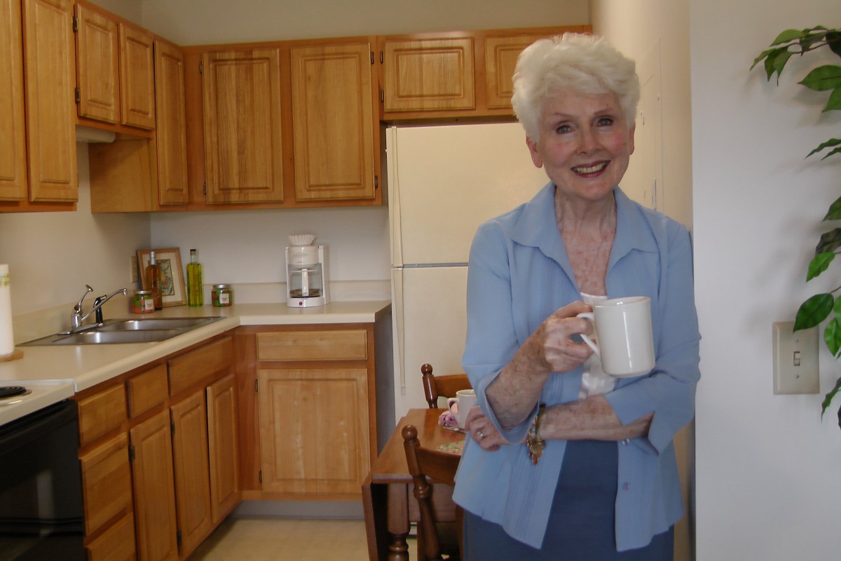 A smiling woman stands in a kitchen holding a coffee cup.