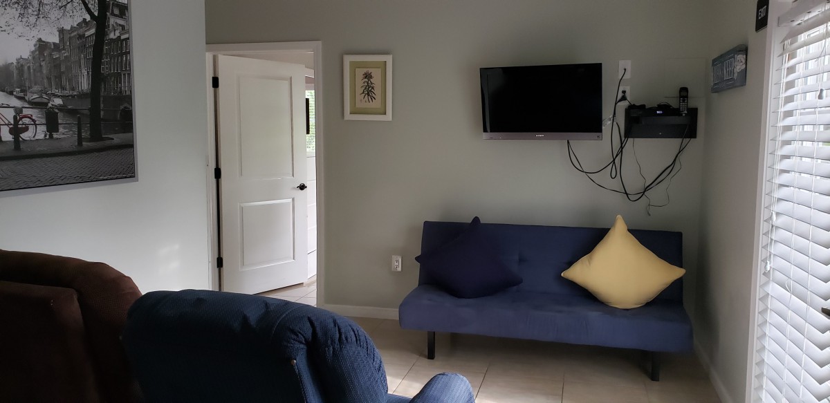 A cozy living room with a blue sofa, cushions, and a wall-mounted television.