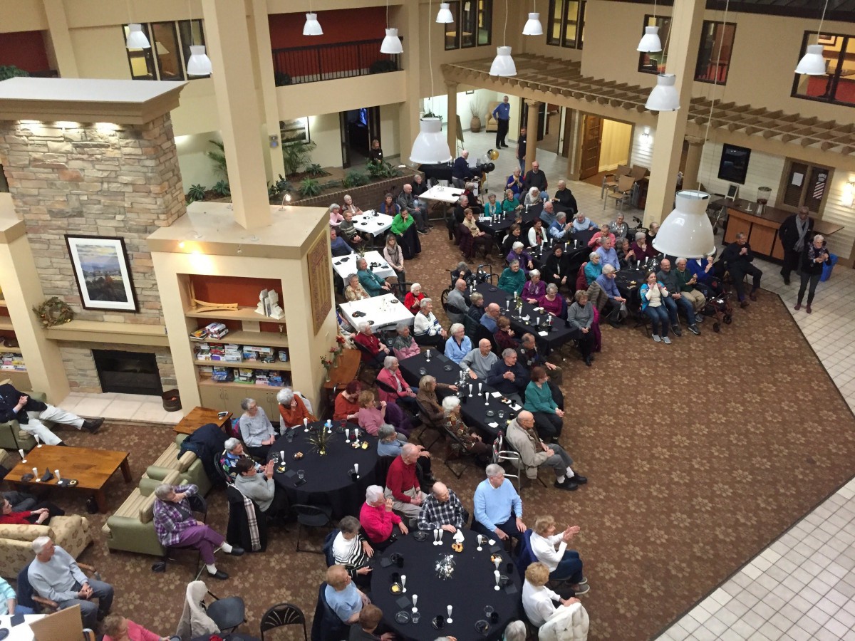 A large group of people seated at round tables in a spacious indoor setting, possibly attending a social event or meeting.
