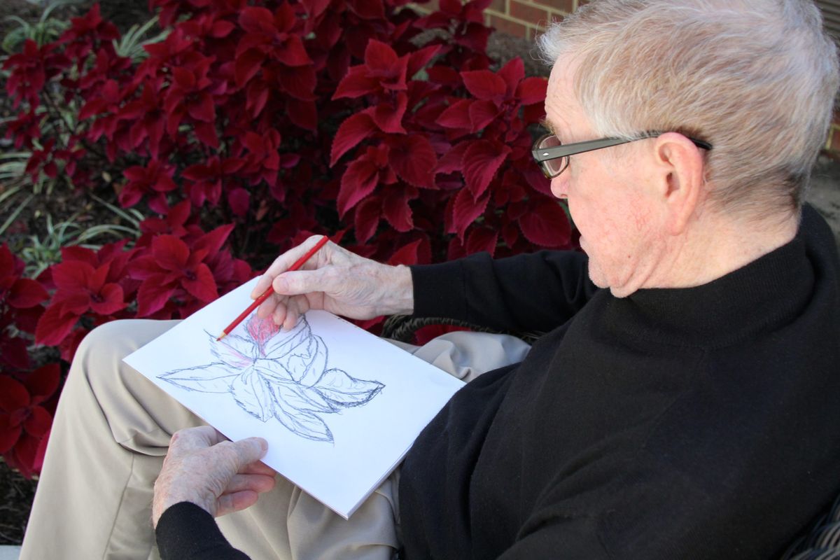 A person sketching a flower while sitting outdoors.