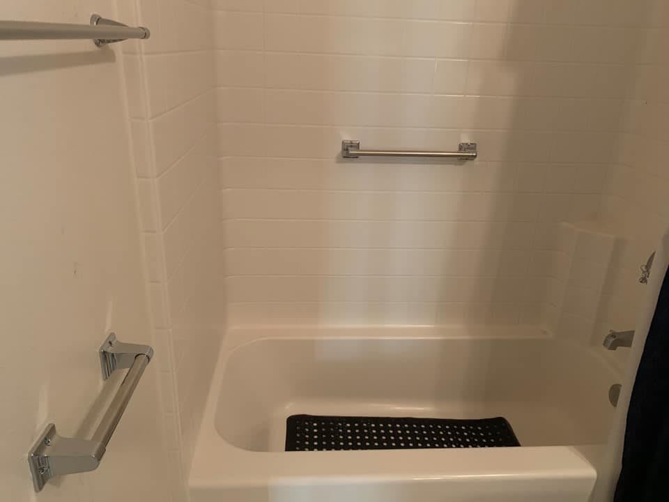 A bathroom with a bathtub-shower combo, featuring a non-slip mat and grab bars.