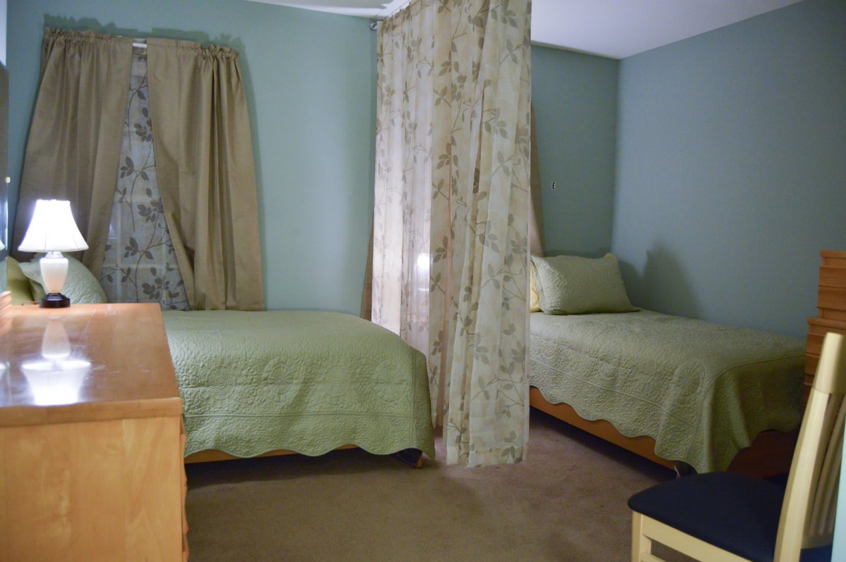 A cozy bedroom with twin beds adorned in green bedding, separated by floral curtains.