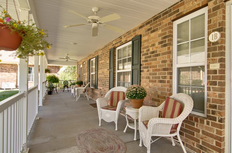 A cozy porch featuring wicker chairs and potted plants against a brick wall.