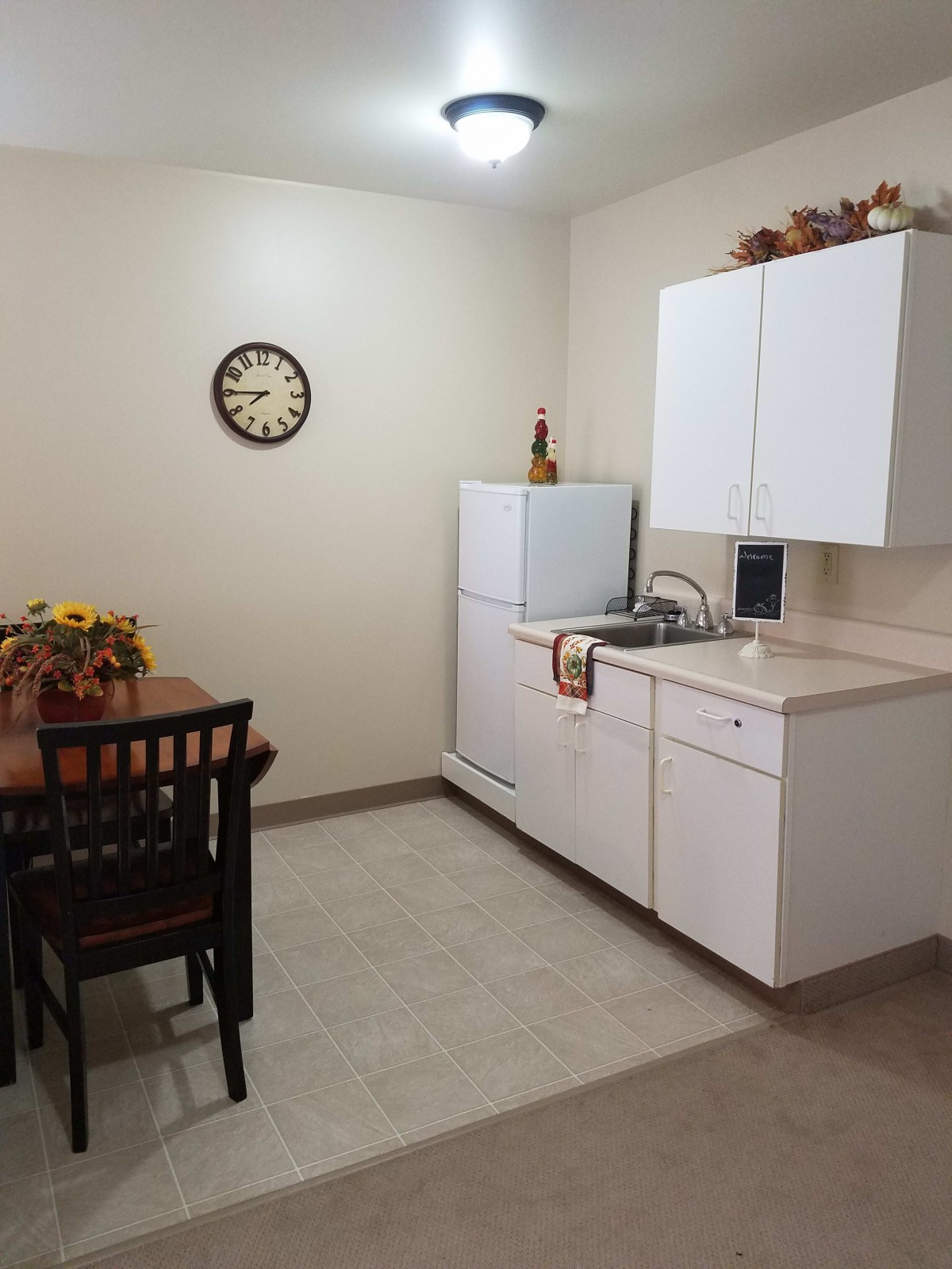 A small kitchen with a dining table, featuring white cabinets and a refrigerator.