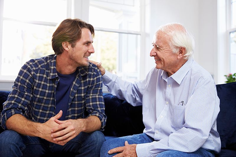 An elderly man and a younger man sharing a warm conversation at home.