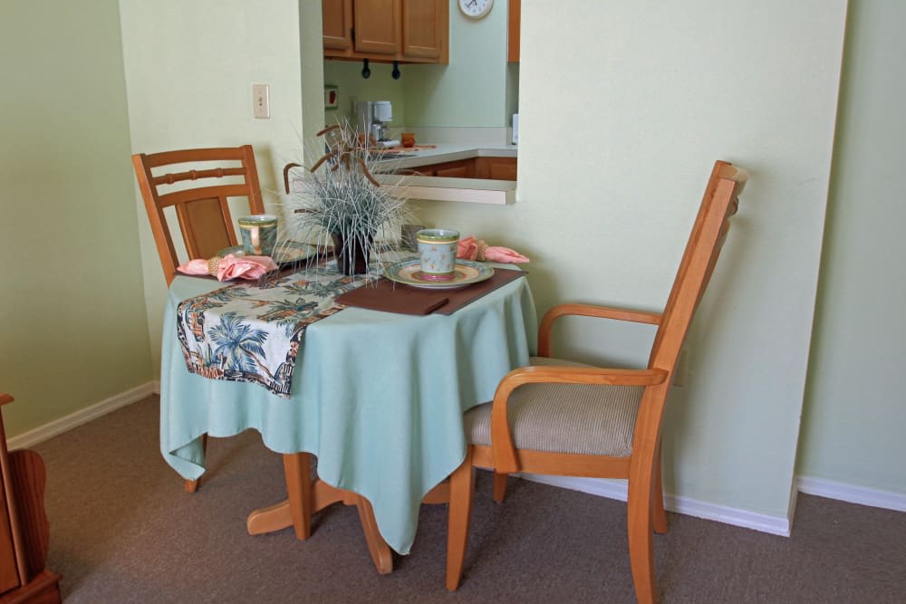 A small dining area with a neatly set table for two, featuring wooden chairs and a light green tablecloth.