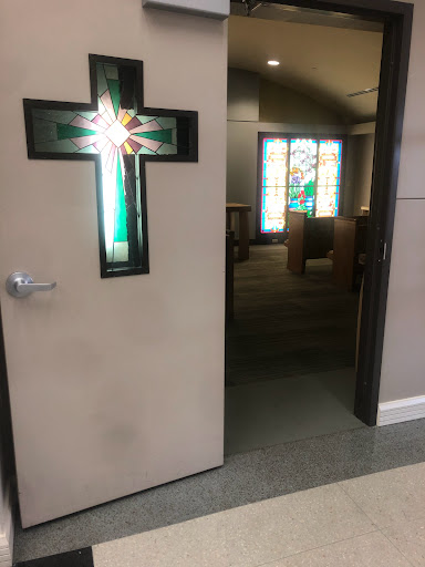 An open church door featuring a cross design, leading into a sanctuary with stained glass windows.