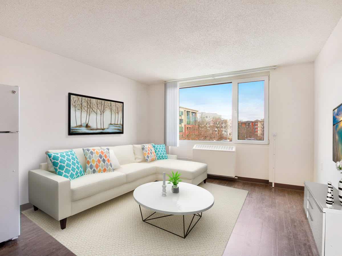 A modern living room featuring a white sectional sofa and a round coffee table, with ample natural light coming through a large window.