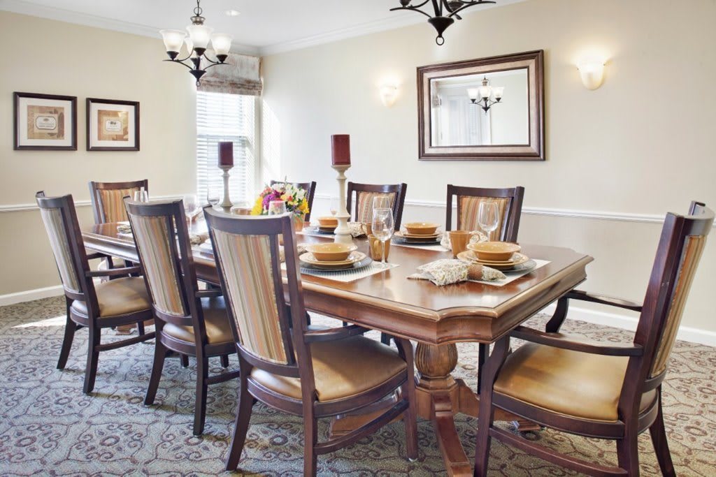 A traditional dining room with a large wooden table set for a meal, surrounded by cushioned chairs and adorned with elegant lighting.