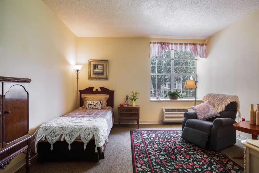 A cozy bedroom with a single bed, armchair, and window adorned with curtains.