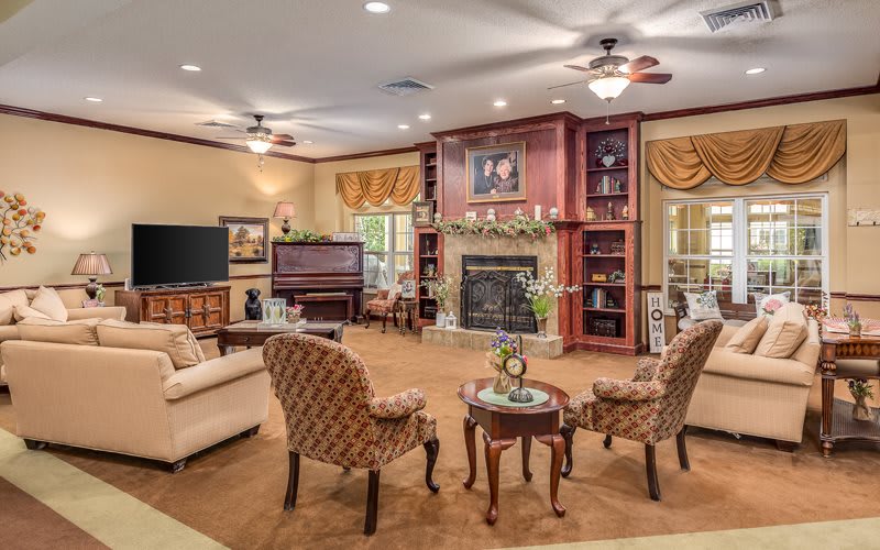 A spacious and elegantly furnished living room featuring a fireplace, seating area, television, and built-in bookshelves.