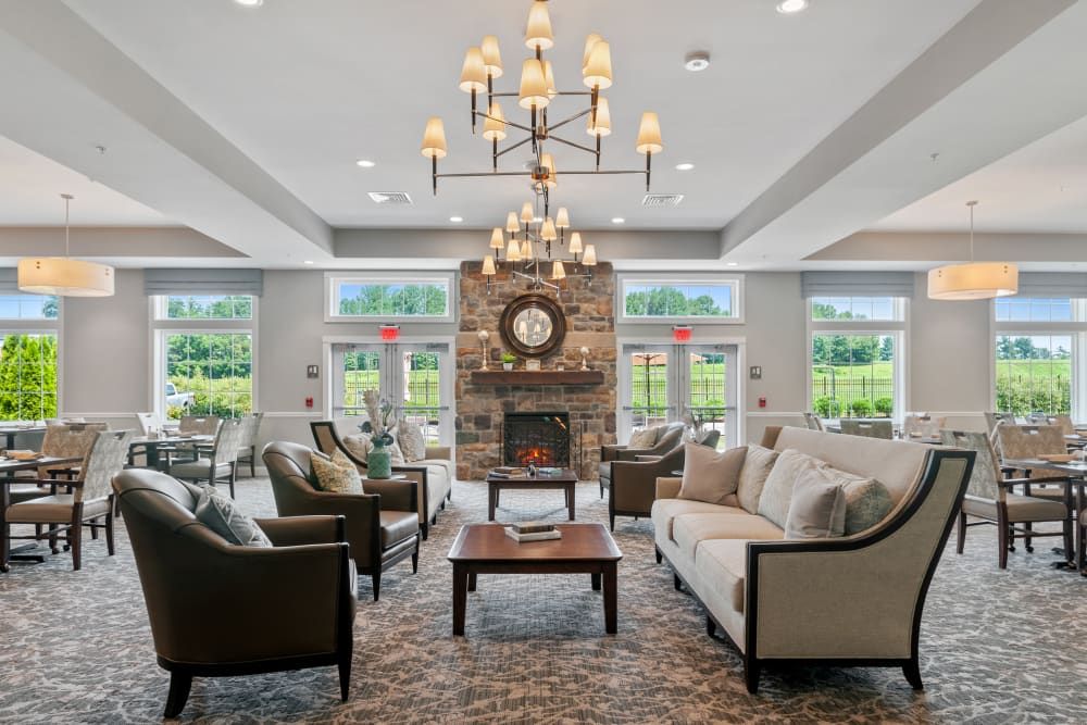 A spacious and elegantly designed living room featuring a large chandelier, comfortable sofas, a fireplace, and ample natural light from multiple windows.