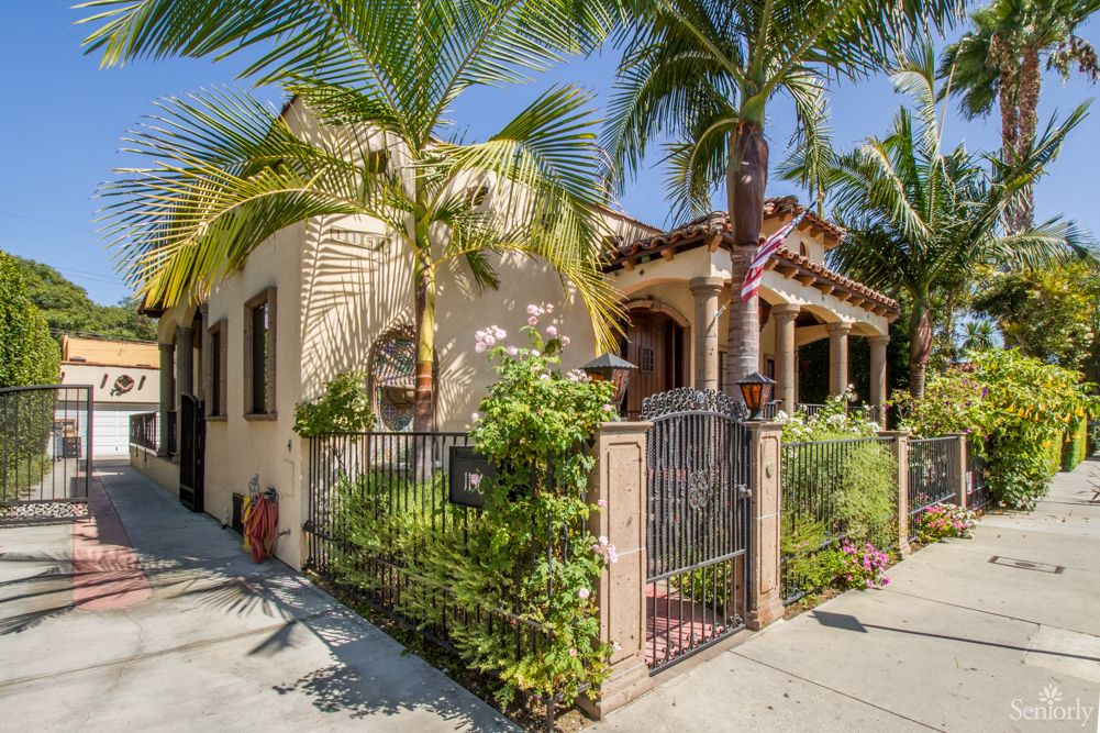 A charming house with a gated garden and lush palm trees basking in the sun.