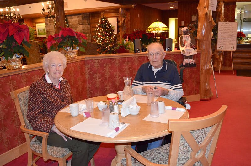 An elderly couple sitting at a table in a restaurant decorated for Christmas.