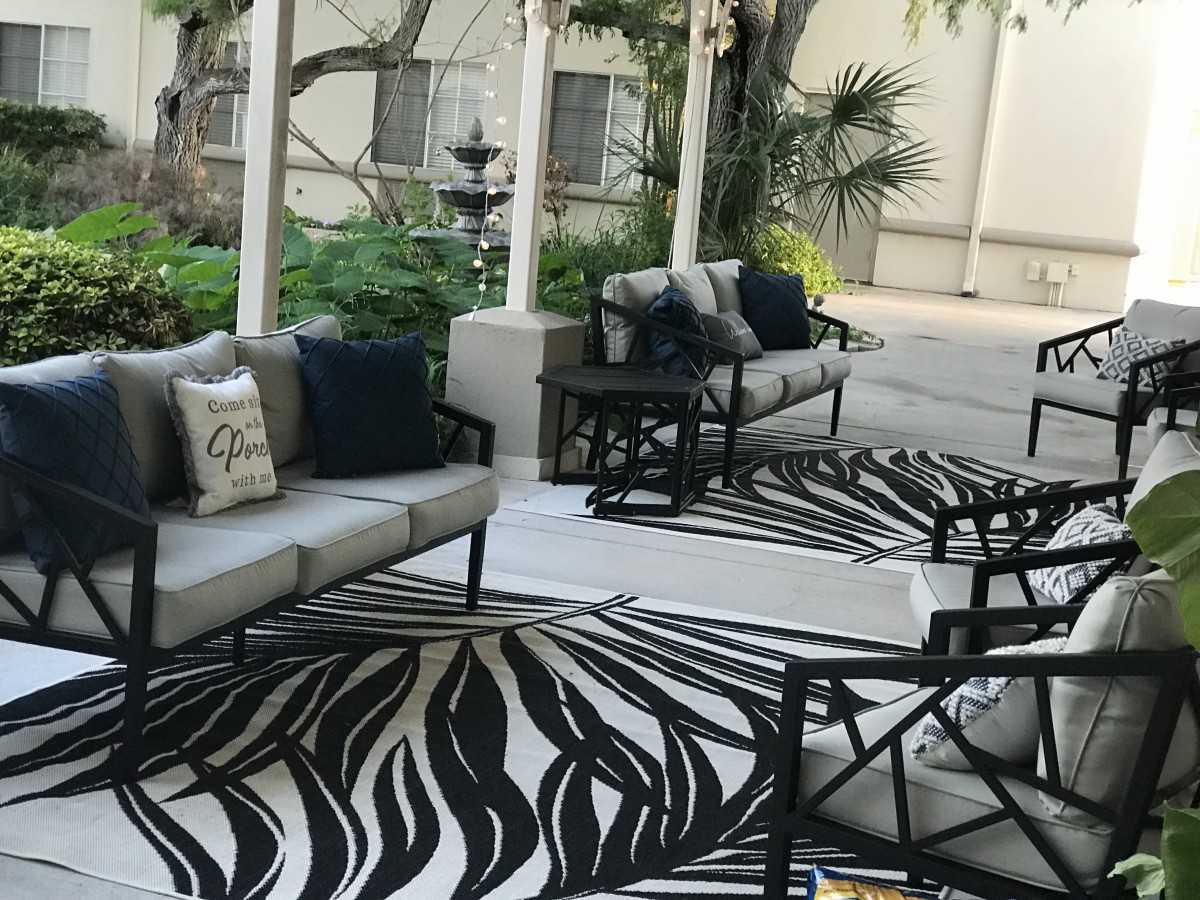 A stylish outdoor patio setup with sofas, chairs, and a patterned rug.