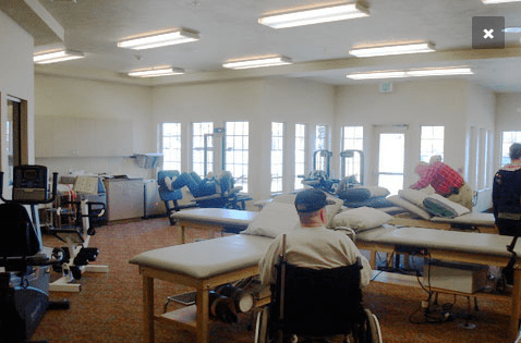 A rehabilitation room with patients in wheelchairs engaging in physical therapy exercises.