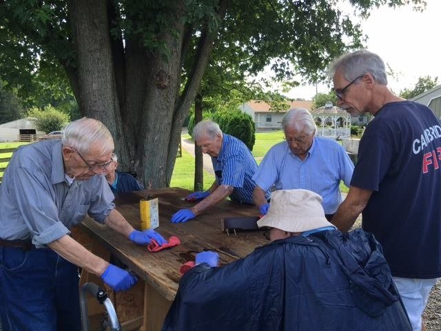 A group of seniors working together on a project outdoors, wearing gardening gloves.
