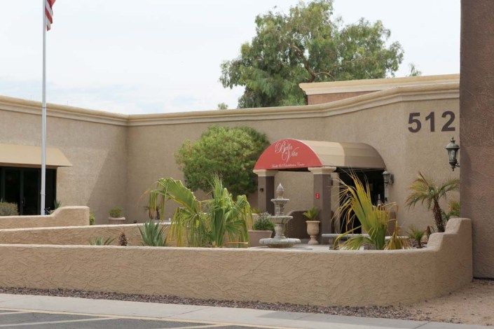 A building with a red awning, surrounded by plants and featuring a fountain.