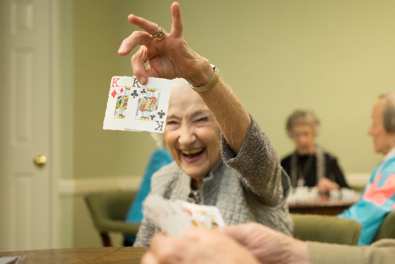 An elderly woman joyfully playing cards indoors.