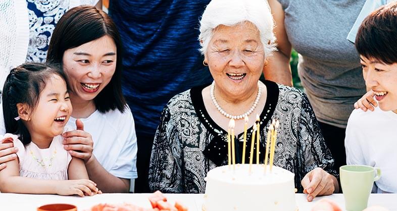 An elderly woman smiles joyfully at her birthday cake surrounded by family.