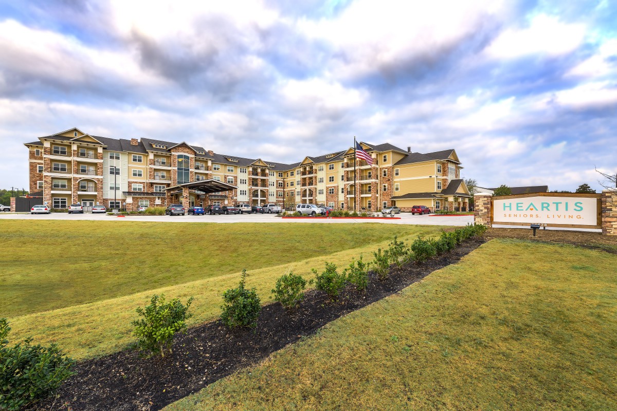 A spacious apartment complex with a well-maintained grassy area and a cloudy sky in the background.