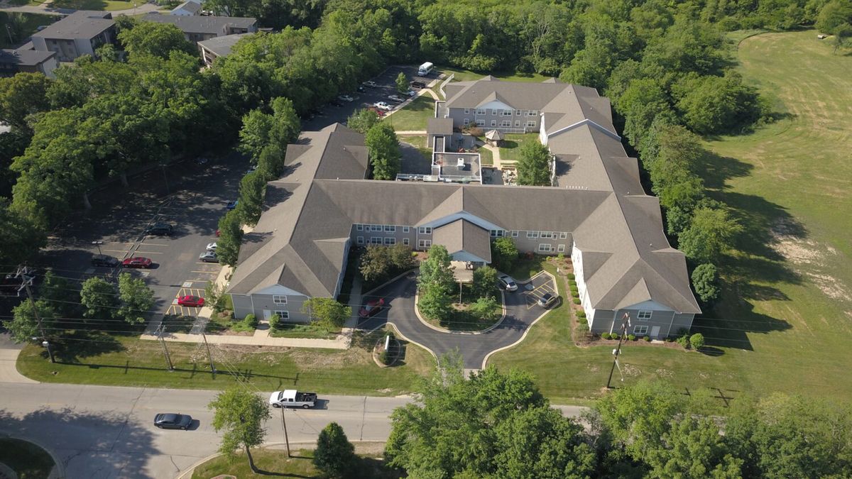 An aerial view of a large building surrounded by trees, with a road and parking area nearby.
